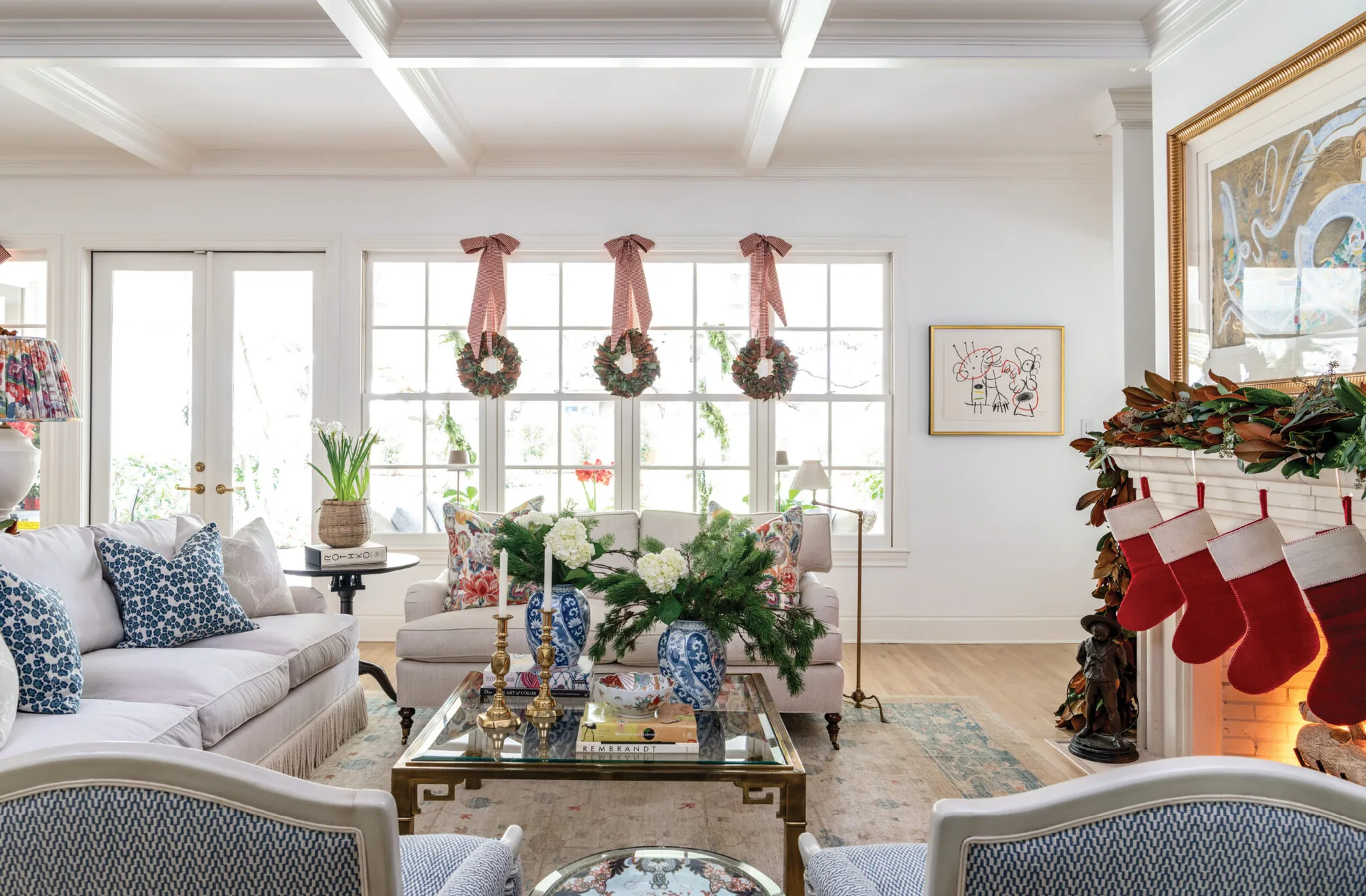 Living room dressed for Christmas with wreaths in the windows, magnolia garland and red stockings on the mantel